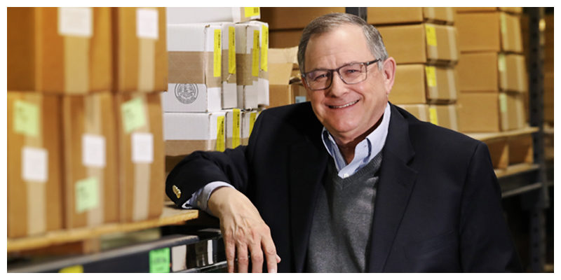 Dean Terry Maness leaning next to a shelf stacked with industrial cardboard boxes